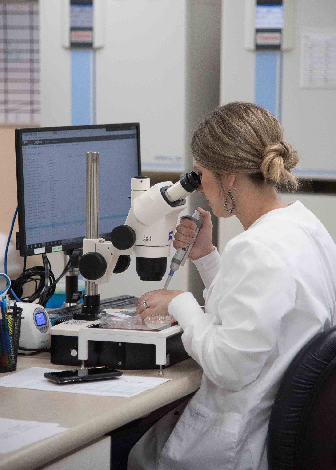 Lab technician using a microscope and pipette while examining samples at a laboratory workstation.